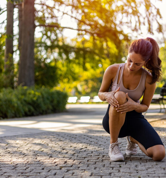Young woman feeling pain in her knee. Woman runner got sports injury running on forest trail. Woman runner hold her sports injured knee.