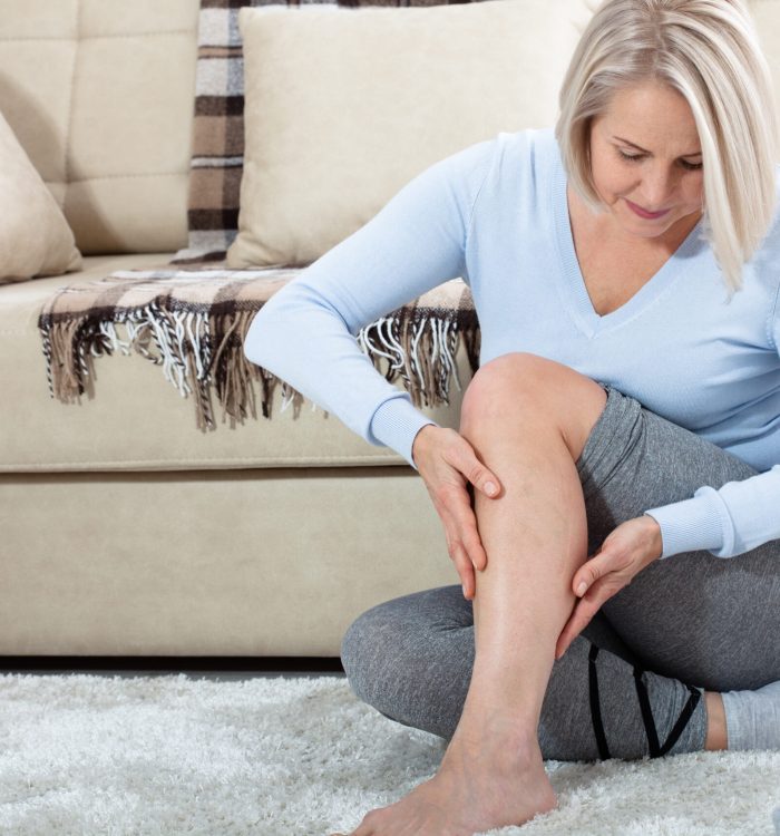 Middle-aged woman suffering from pain in leg at home, closeup. Physical injury concept. Ankle pain, painful point.