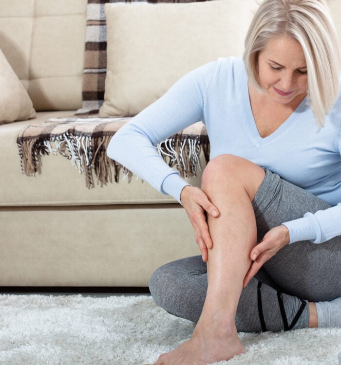 Middle-aged woman suffering from pain in leg at home, closeup. Physical injury concept. Ankle pain, painful point.