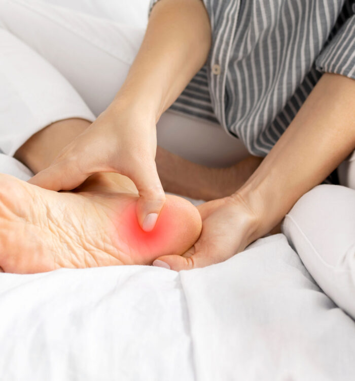 Young woman feeling pain when she press on heel and foot while sitting on the bed at home. Painful female legs from wearing uncomfortable tight shoes and high heels, sprain, arthrosis. Health concept.
