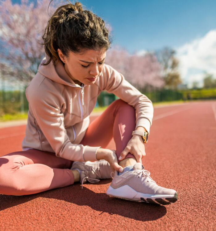 Young female athlete having leg pain. She injured her ankle while running on sports track.