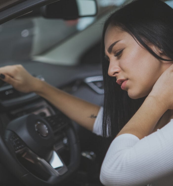 Beautiful young woman rubbing her neck, feeling sore after long drive. Female driver having terrible neck pain after whiplash injury in car crash. Healthcare, safety, pain concept